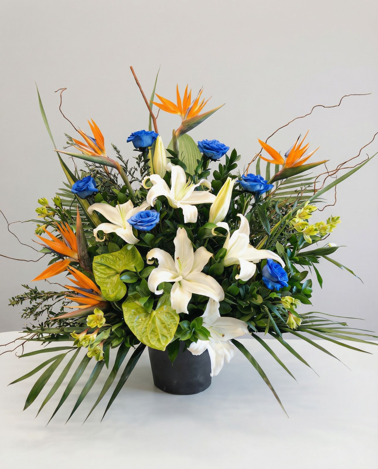 Corbeille funéraire spectaculaire composée d’oiseaux du paradis, de lys, d’anthuriums et de roses bleues. Cette création florale audacieuse et contemporaine rend un hommage distinctif et mémorable, symbolisant force et sérénité.