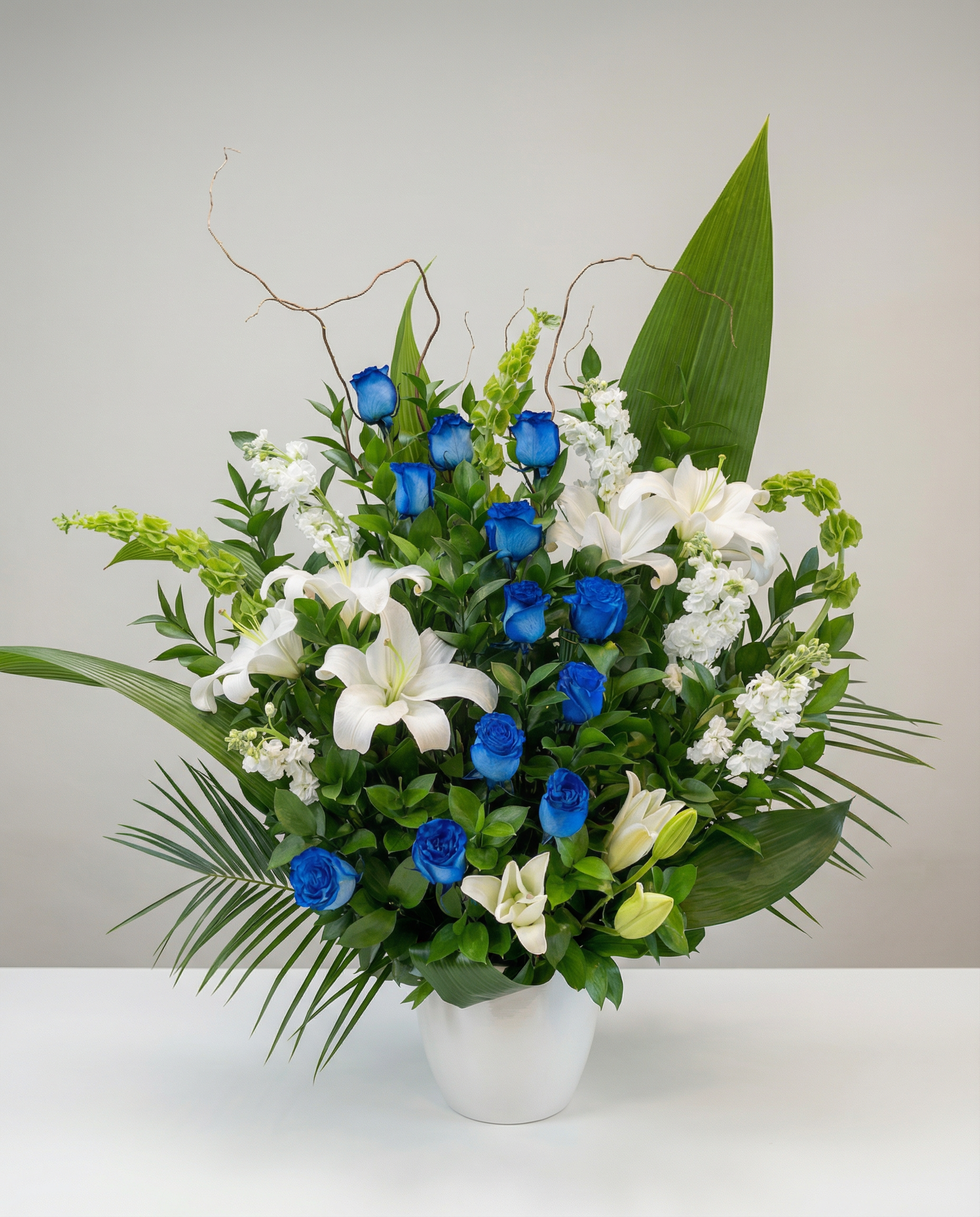 Arrangement de sympathie composé de roses bleues, de lys oriental et de mufliers, créant un contraste floral à la fois moderne et apaisant. Cette corbeille funéraire exprime un message de soutien profond et de respect sincère.